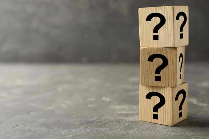 Three wooden blocks with black question marks stacked.