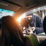 Masked criminal reaching through car window attempting to rob occupants inside vehicle on rainy day