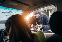 Masked criminal reaching through car window attempting to rob occupants inside vehicle on rainy day