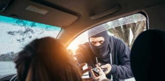 Masked criminal reaching through car window attempting to rob occupants inside vehicle on rainy day
