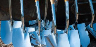 A collection of shiny metal shovels with wooden handles arranged on the ground