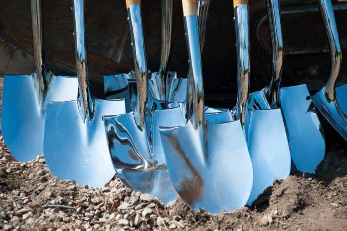 A collection of shiny metal shovels with wooden handles arranged on the ground