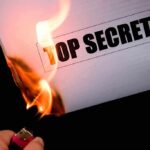 A hand holding a lighter igniting a paper labeled TOP SECRET as it catches fire