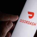 A hand holding a smartphone displaying the Doordash logo