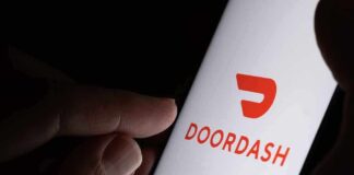 A hand holding a smartphone displaying the Doordash logo