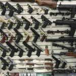 Prison Badge Loophole: Guns Without Checks? Wall display with handguns and rifles for sale.