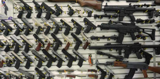 Prison Badge Loophole: Guns Without Checks? Wall display with handguns and rifles for sale.