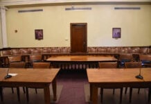 Empty courtroom with wooden tables, chairs, and a door.