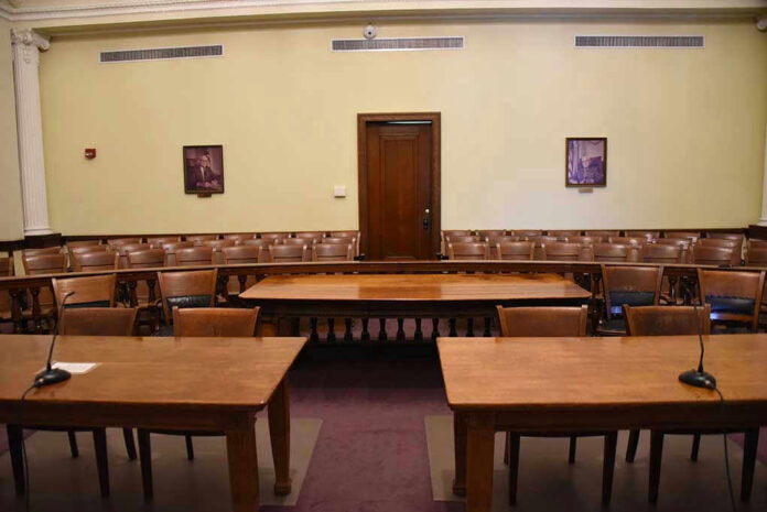 Empty courtroom with wooden tables, chairs, and a door.