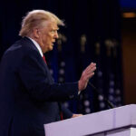 Person speaking at a podium with hand raised