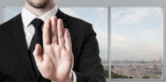 Person in suit with hand raised in stop gesture.