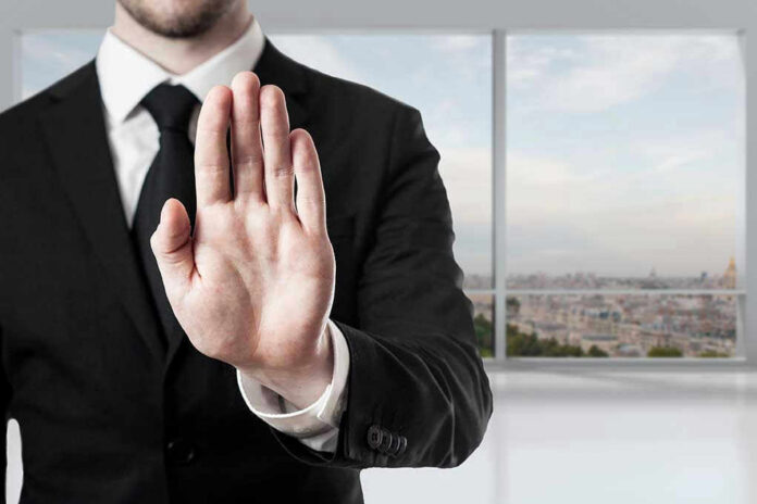 Person in suit with hand raised in stop gesture.