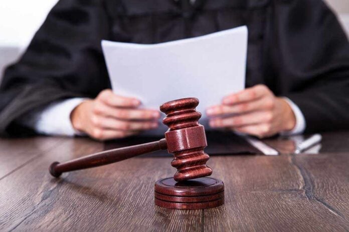 Close-up,Of,Male,Judge,In,Front,Of,Mallet,Holding,Documents A judge holding documents with a gavel in the foreground