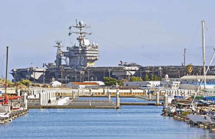shutterstock_194774165 A large naval aircraft carrier docked in a harbor with smaller boats in the foreground