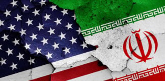 Iran “Suspends” Talks as U.S. Says Negotiations Continue Cracked American and Iranian flags painted on a wall.
