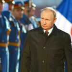 Man in black coat with soldiers in background.