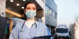 Ebola Surge Raises Global Health Concerns Nurse in scrubs and mask outside hospital holding clipboard.
