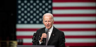Man speaking at podium with US flag background.