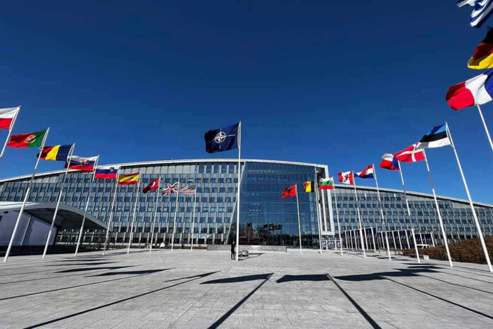 Flags outside NATO headquarters building under clear blue sky.