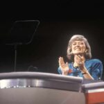 Energy Bills Surge as Britain Feels Global Fallout A female speaker on stage smiling and clapping during a presentation