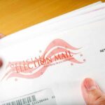 A hand holding an envelope labeled Official Election Mail