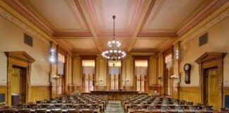 Intelligence Office Cuts Bloat by 40% Interior view of a historic courtroom with wooden furnishings and chandeliers