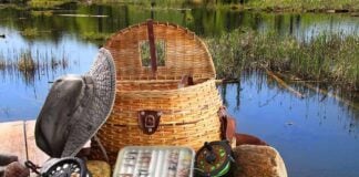 Fishing gear including a hat, basket, and fishing rods arranged by a serene water body
