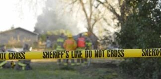 Fireworks Stockpile Turns Homes Into War Zone Yellow police tape marking a restricted area at a fire scene with firefighters in the background