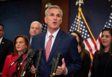 Man speaking at a press conference with American flags.