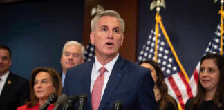 Man speaking at a press conference with American flags.