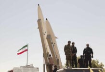 Iran’s Power Transition Faces New Mystery Military personnel beside missiles and Iranian flag.