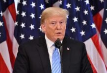 A man speaking at a podium with American flags in the background