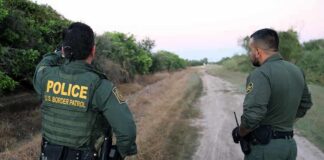 Two uniformed officers stand on a rural dirt road