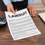Person holding a lawsuit document on a wooden desk