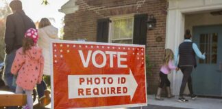 Red voting sign with arrow near people entering a polling place