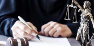 Judge writing at desk with gavel and Lady Justice statue