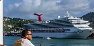 Man leaning on ship railing looking at a docked cruise ship