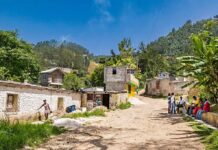 Family Trapped: American Flies to West Bank Rural village street with people gathered and hills in the background