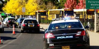 Police cars with flashing lights near school buses on a city street
