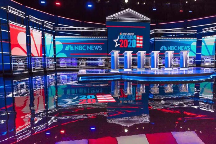 Televised debate stage with multiple podiums and bright red, white, and blue lighting