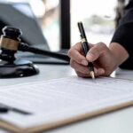 Defense Intelligence Insider Pleads Guilty Hand signing legal document beside gavel and laptop
