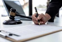 Hand signing legal document beside gavel and laptop