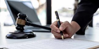 Hand signing legal document beside gavel and laptop