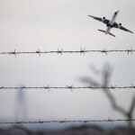 Airplane taking off above barbed wire fence