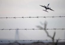 Airplane taking off above barbed wire fence