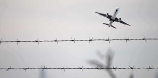 Airplane taking off above barbed wire fence