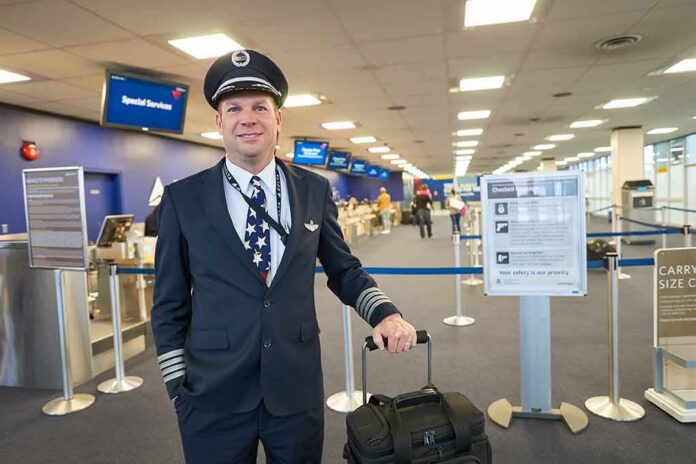 shutterstock_433291228 Airline pilot standing in airport check-in area with rolling bag