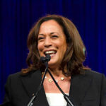 Donor Calls Raise Questions: “We’ll Win” Smiling woman speaking at a podium with microphones.