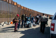 Migrant Caravan Heads Toward U.S. Border Group of people standing by a border fence with officers and vehicles