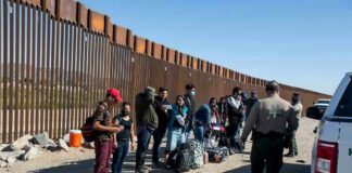 Migrant Caravan Heads Toward U.S. Border Group of people standing by a border fence with officers and vehicles